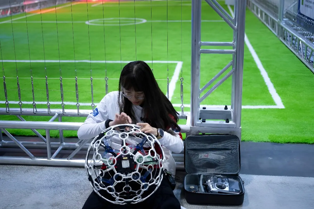 Competitor inspecting a full-size competition drone soccer ball beside the arena