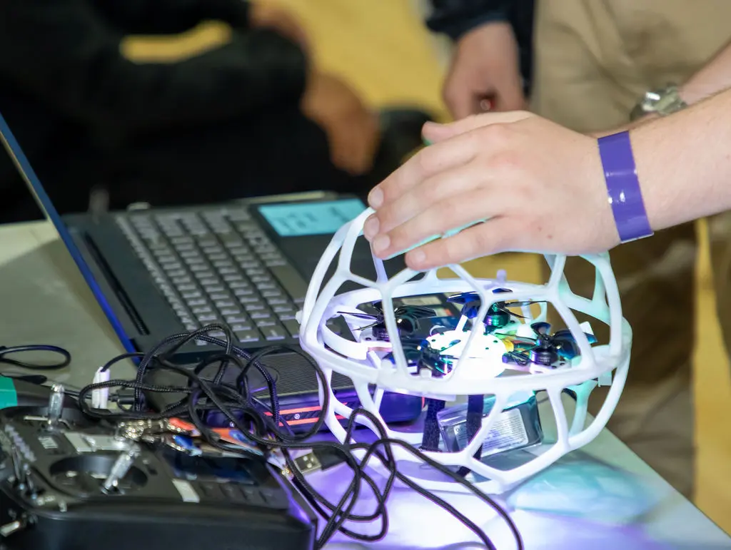 Student preparing a protected soccer drone beside its controller and computer